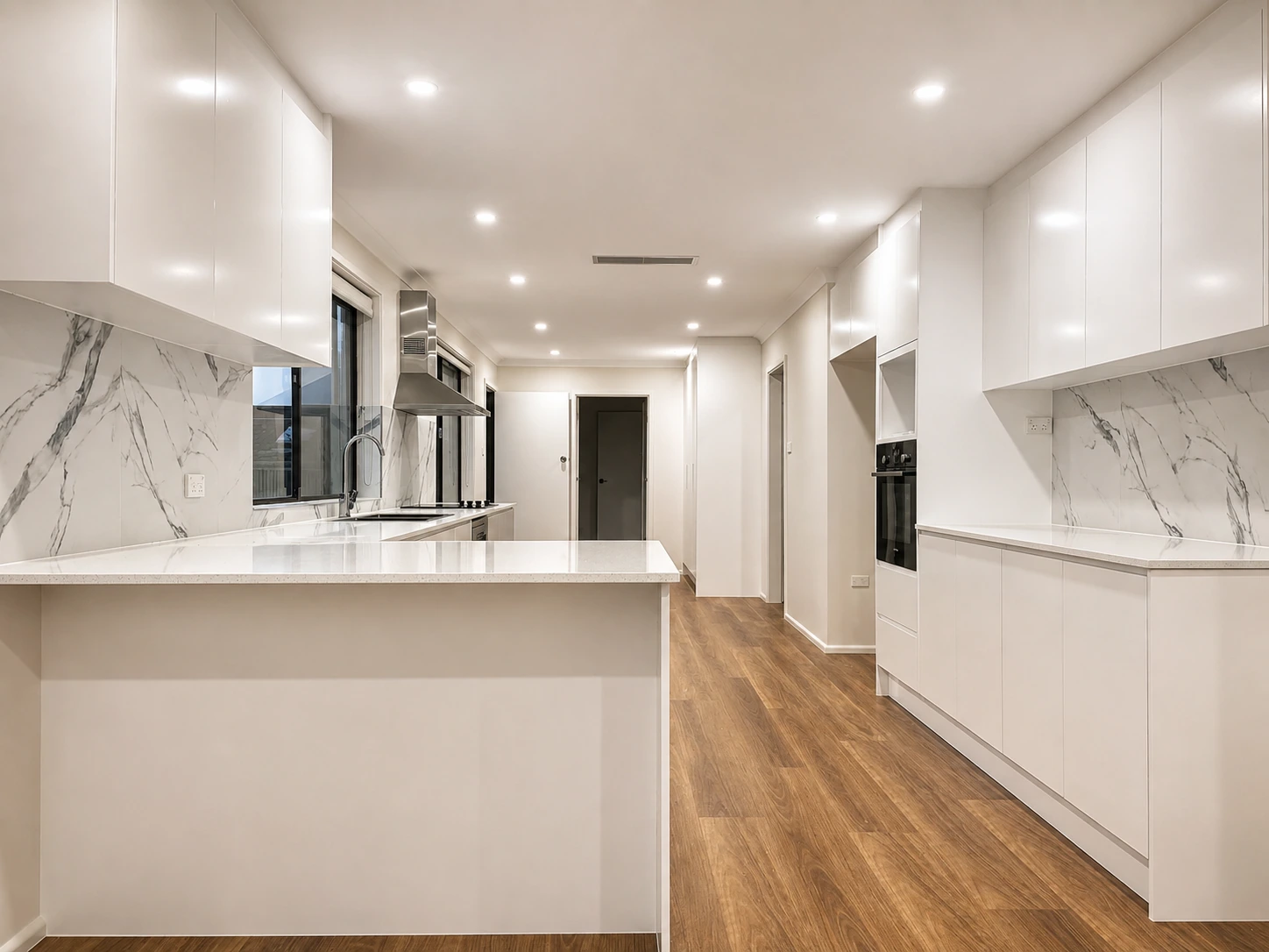 Contemporary kitchen renovation in Castle Hill — U-shaped peninsula and a run of full-height handleless joinery with a black built-in oven, a stainless chimney rangehood and warm timber-look flooring